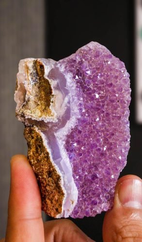 Detailed view of a purple amethyst geode crystal held between fingers, showcasing natural beauty.
