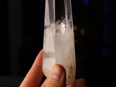 Home Close-up of a hand holding a clear quartz crystal tower against a dark background.