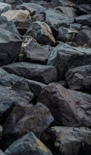 From above of rough dark stones placed on shore in nature in daytime